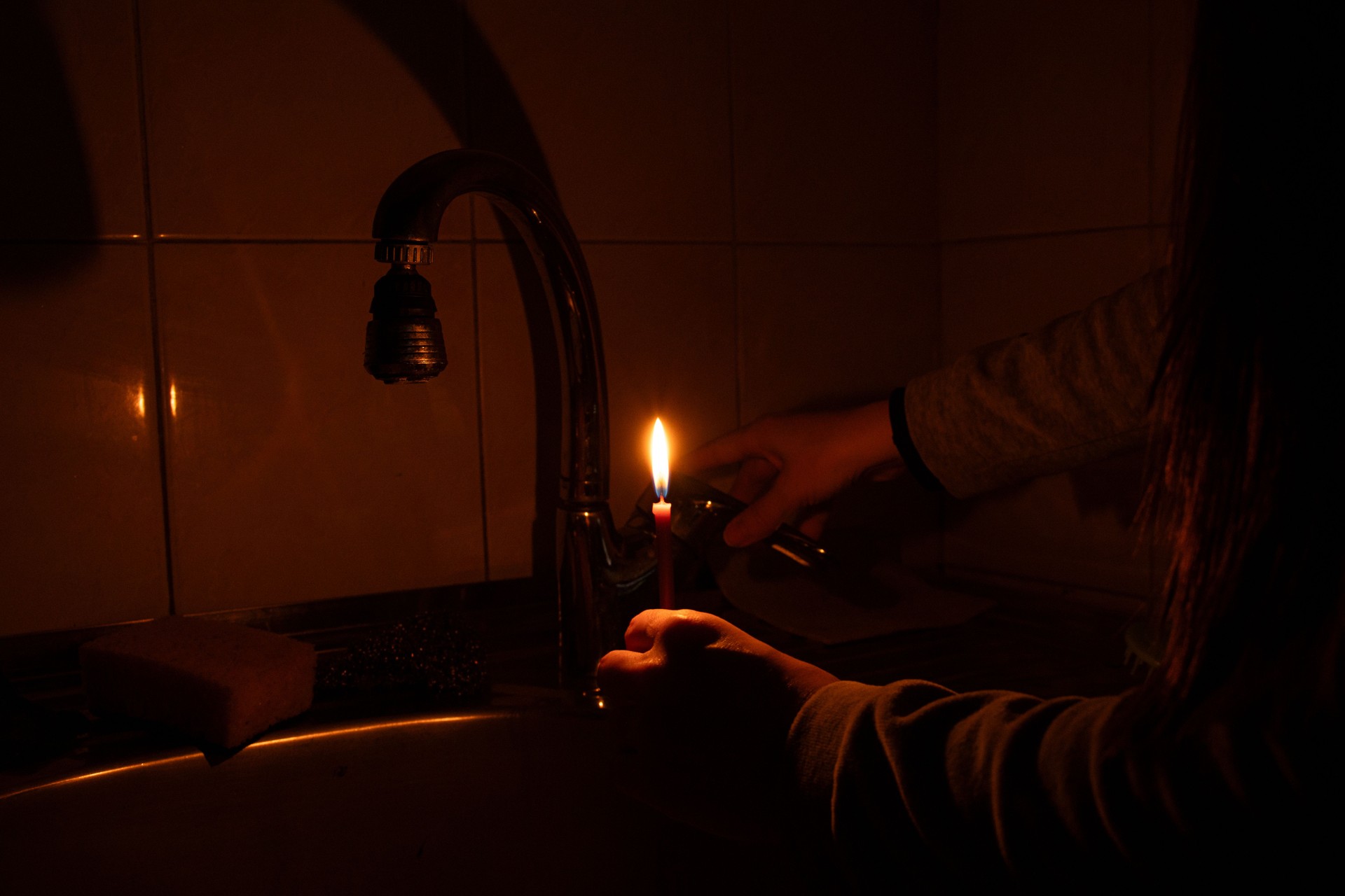 Girl checking tap by candle during blackout